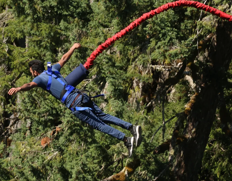 A jumper falling through the forest on a red bungee cord in Rishikesh